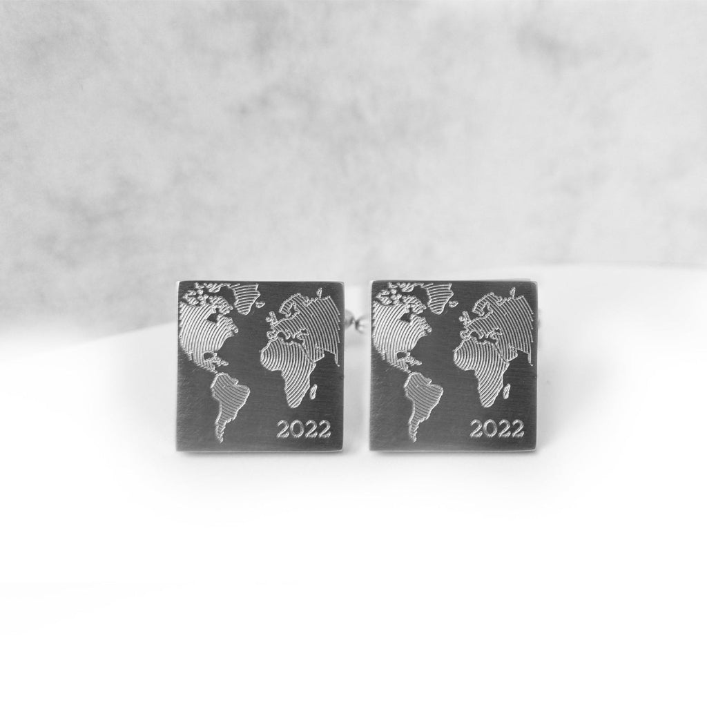 Quadratische Edelstahl-Manschettenknöpfe mit eingraviertem Weltmotiv und Datum, frontale Ansicht.