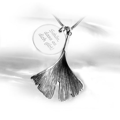 Silberkette mit zwei Anhängern: einem filigranen Ginkgoblatt und einer runden Gravurplatte mit dem Spruch „Schön, dass es dich gibt!“.