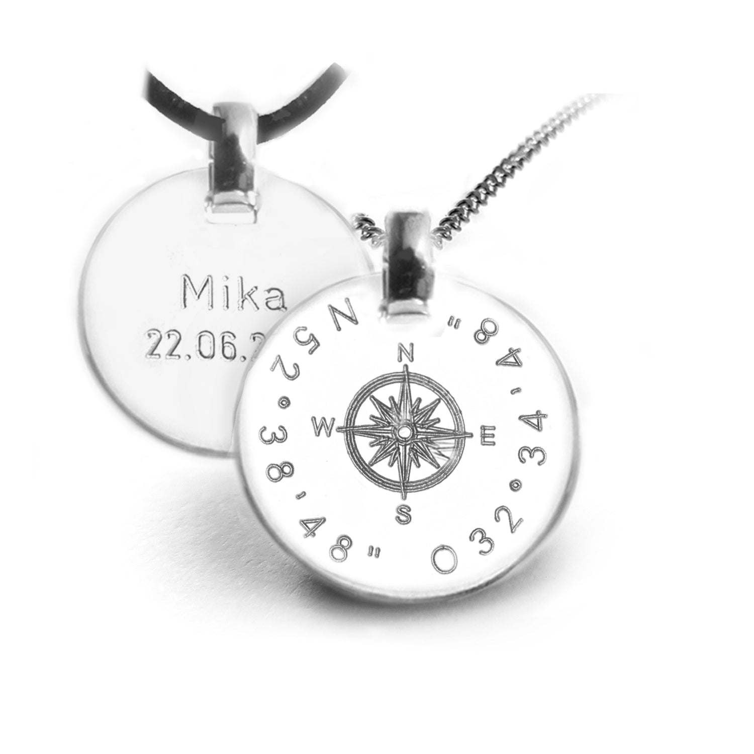 Das Foto zeigt zwei Kompass-Ketten: vorne eine Silberkette mit Kompass-Anhänger und gravierten Koordinaten, hinten eine Lederbandkette mit Beispielgravur auf der Rückseite.