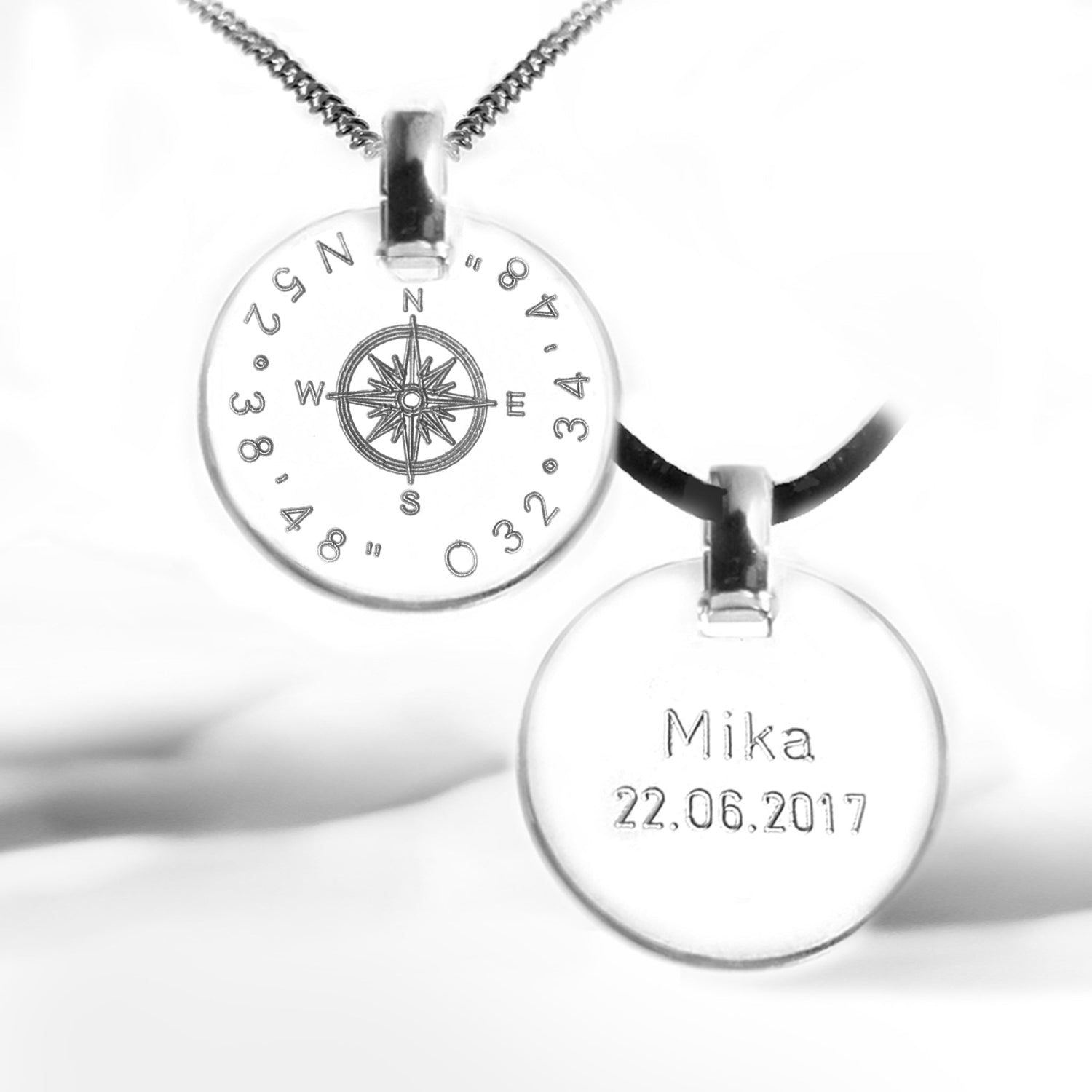 Zwei Halsketten: eine Silberkette mit Kompass-Anhänger und gravierten Koordinaten sowie eine Lederbandkette mit Beispielgravur auf der Rückseite