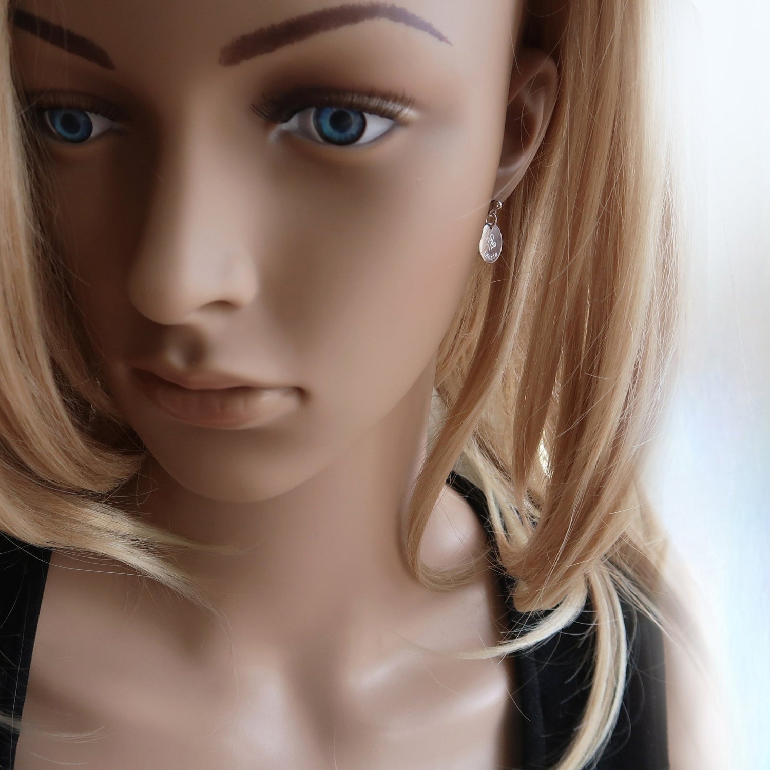 Eine Frau trägt Ohrringe aus 925er Sterlingsilber mit einem eingravierten Namen und zwei Herzen