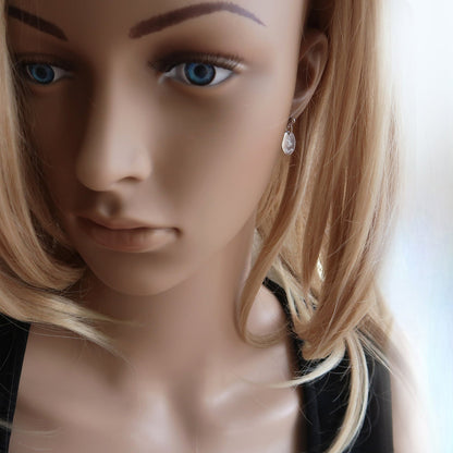 Eine Frau trägt Ohrringe aus 925er Sterlingsilber mit einem eingravierten Namen und zwei Herzen