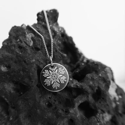 Silberner Schneeflocken-Anhänger hängt kontrastreich an dunklem Felsen.