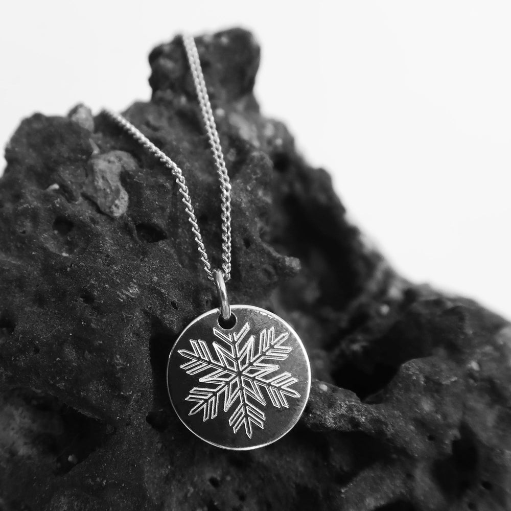 Filigrane Schneeflocken Kette aus Silber auf schwarzem Felsen inszeniert.