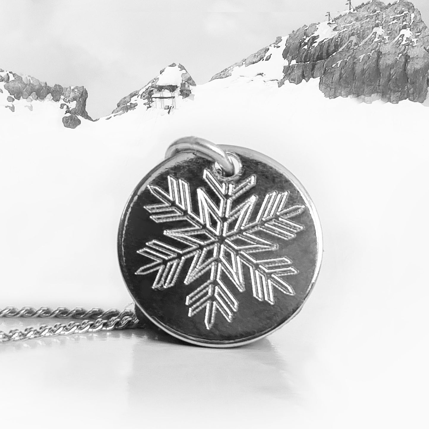 Feine Silberkette mit rundem Schneeflocke Anhänger auf winterlichem Hintergrund.