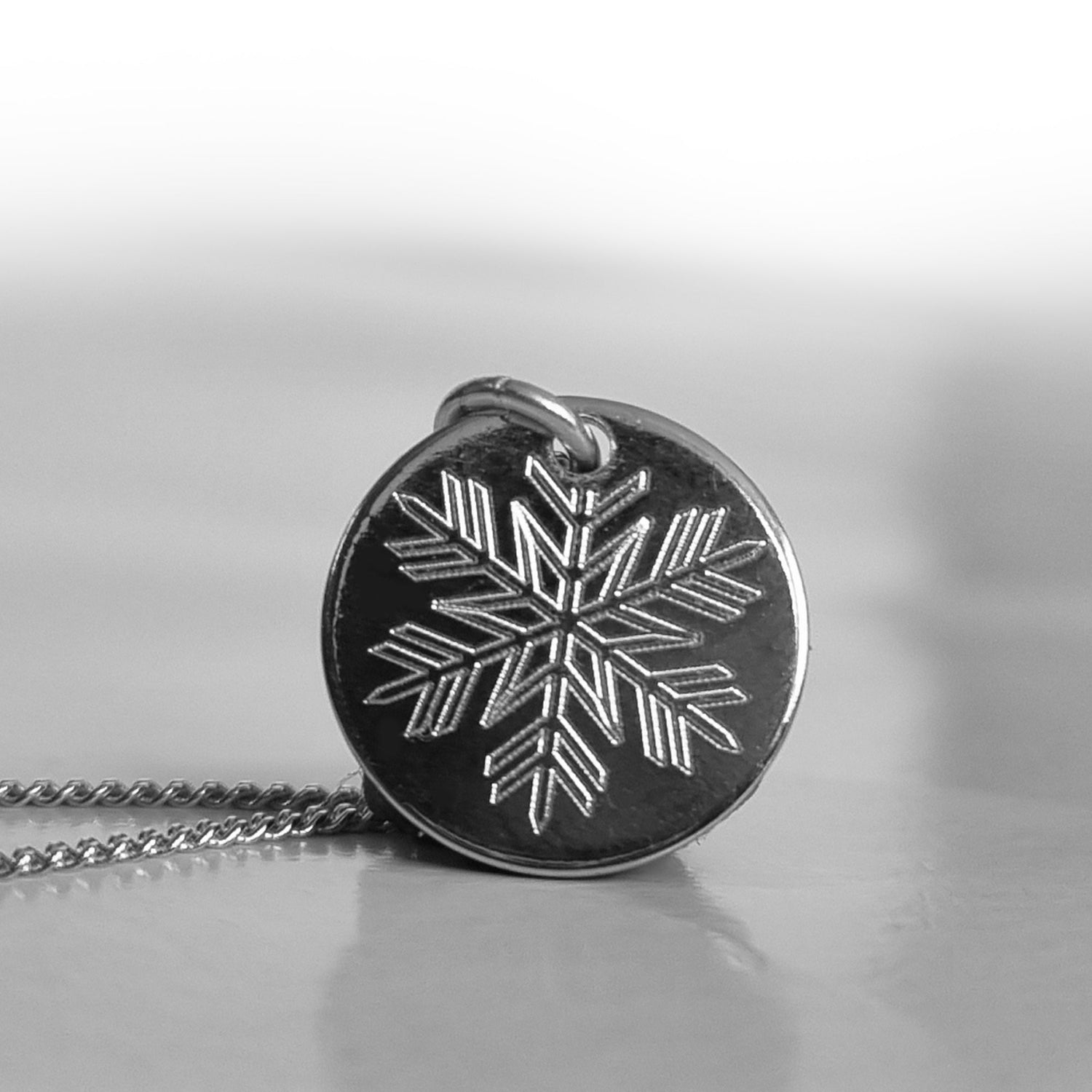 Runder Schneeflocken-Anhänger mit einer rhodinierten Silberkette auf neutralem Hintergrund