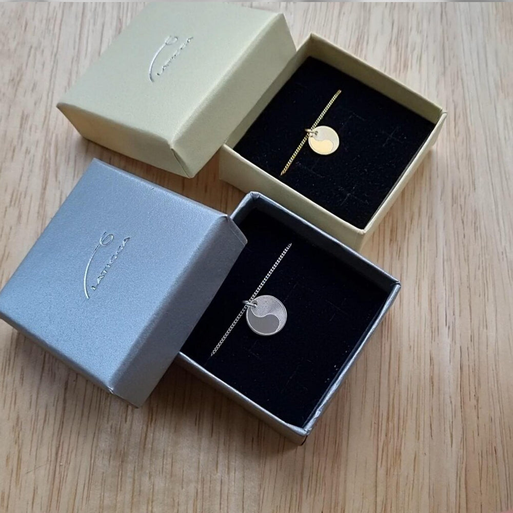 Zwei Yin Yang Ketten mit Anhänger – eine aus Silber, eine vergoldet, präsentiert in Geschenkbox.